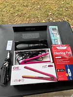 José Eber curling iron, CHI hair straightener, king size heating pad and pet grooming brush on black surface outdoors