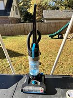 Full view of black and blue Bissell upright vacuum cleaner, showing handle, dust canister, and cleaning head.