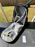 Open view of black padded camera backpack showing front flap with mesh pockets and yellow trim, resting on a surface outside.