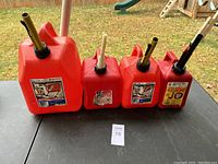 Four red plastic gas cans of varying sizes arranged on a table outdoors, showing the full lot.
