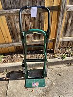 Front view of the green metal hand truck with black padded handles and folding toe plate with American flag sticker.