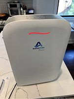 Front view of the white Alexapure Breeze HEPA air purifier with control buttons on top, placed on a kitchen counter.