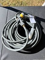 Full view of the coiled gray water hose with an attached yellow and black adjustable spray nozzle.