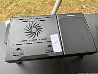 Top view of the laptop desk showing ventilation slots and central fan with attached mouse pad area, black plastic build.