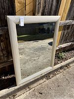 Full view of large rectangular mirror with gold-colored textured frame leaning against wooden fence outdoors.