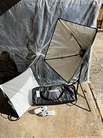 Photography lighting equipment kit set up on the ground. Softbox fully open with reflective silver interior. Adjustable tripod stand attached. Two compact fluorescent bulbs and a carrying bag placed beside stand.