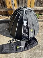 Large black dome-shaped photography softbox with white ribs standing upright outdoors, next to a black carry bag