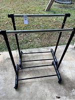 Pair of black and chrome apparel racks on a concrete floor outside, showing adjustable heights and wheels.