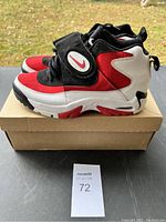 Left side view of the right shoe showing color blocking and Nike branding on the strap and sole, shoe rests on cardboard box outdoors.