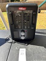 Front view of black Hyper Tough electric space heater with grille and two control knobs, power indicator light visible, placed on a table outside.