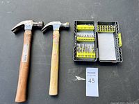 Two claw hammers and an open case with drill bits organized in rows, placed on a black surface.