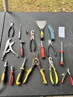 Hand tools spread out on a table including pliers, scrapers, cutters, and screwdrivers.