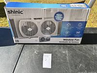 Photo of unopened Shinic window fan box laid flat on a table outdoors.