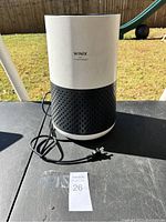 Photo of full Winix air purifier showing cylindrical design, color, and power cord on black table outdoors.