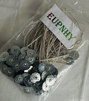 Clear plastic bag containing about 50 white cotton candle wicks with attached round silver metal tabs, branded EUPNHY on label