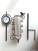Copper rain gauge with vertical measuring tube covered in bubble wrap, includes large black number scale for inches and metal bird decoration above, thermometer attached on the side.