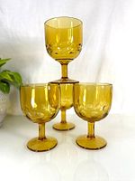 Four amber glass heavy goblets, three with identical dotted design and one with a different raised dot pattern, arranged with one goblet on top of the other three. Shows shape, color, and size.