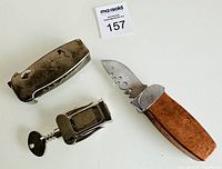 Shows two pocket knives and a corkscrew arranged on a white surface with auction lot number card