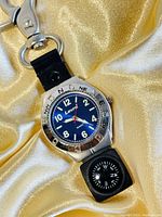 Front view of Levi's quartz watch on black strap with compass keychain attached, silver-tone stainless steel case, blue dial with white numerals and red second hand, rotating bezel with compass directions.