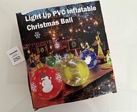 Box front showing the product name 'Light Up PVC Inflatable Christmas Ball' and a display of five colored inflatable balls lit up in a night outdoor setting.