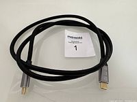 Full view of the black braided USB Type-C to USB Type-C angled cable coiled on white surface with a MaxSold tag.