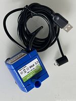 Photo showing the blue submersible water pump with attached USB power cable coiled around it.