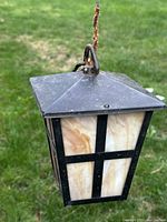 Front and side angled view of the antique Mission Arts and Crafts slag glass hanging shade outdoors with garden background.