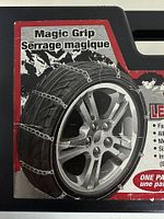 Box art showing a car tire wrapped with Magic Grip cable link snow chains in front of mountain background, illustrating chain pattern and use.
