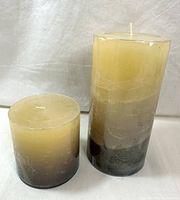 Two pillar candles, one taller and one shorter, with gradient color from beige to dark gray/black.