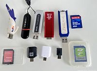 Photo showing five USB flash drives in various colors and brands along with USB adapters and two SD cards on white background.