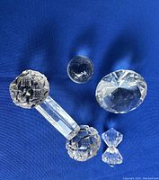 Six crystal knife rests on blue background, showing variety of shapes including spheres, cylinder with ends, diamond shape and hourglass shape.