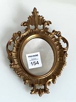 Front view of the vintage oval wall mirror showing the ornate gold-toned frame with detailed leaf and scroll motifs.