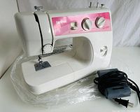 Front and side view of white and pink Brother LS-2020P mechanical sewing machine with foot pedal and power cord on white surface with plastic wrapping.