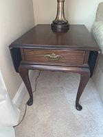 Side view of one dark wood Ethan Allen end table with a lamp on top, showing drawer with brass handle and one drop leaf extended downward