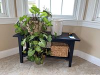 Full view of black wooden bench with decorative plant in patterned pot, white mason jar, and woven basket on lower shelf