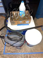 Photo showing Craftsman vacuum, mason jars in box, white cleaning product bottle, and ice melt bucket on floor.