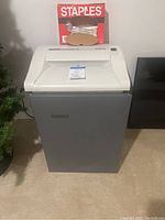 Front view of the Fellowes commercial paper shredder with Staples trash bag box on top.