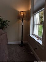 Full view of the floor lamp turned on standing in a corner by the window.