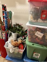 View of stacked plastic bins with fall pumpkin decor and other holiday items, a white ceramic pitcher with faux greenery and pinecones, and plastic bags.