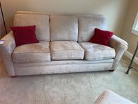 Front view of beige La-Z-Boy sofa with three seat cushions and two red pillows