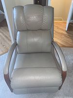 Front view of tan/taupe synthetic leather armchair showing padded back, seat, wood arms and circular base