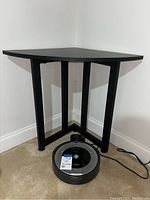 Black wood corner table placed in a carpeted room corner, showing triangular top and metal legs.
