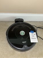 Top view of black iRobot Roomba 675 vacuum along with charging base on beige carpet.