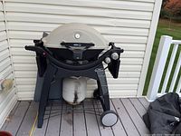 Full view of Weber Q gas grill on deck with propane tank (not included) positioned below and black cover placed nearby.