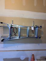 Full view of folded Werner aluminum ladder with bungee cords hanging on hooks in garage.
