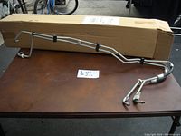 View of two bent metal transmission lines displayed on table with their original box in background.