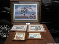 Group photo of all five framed duck lithographs including one large and four smaller prints on a table.