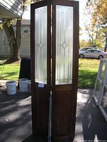 Front view of the wooden bi-fold door showing the two panels with frosted glass decorated with gold geometric trim.