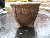 Front view showing decorative grape cluster design and three short legs.