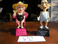 Front view of both bobbleheads showing details of clothing, colors, poses, and bases with text.